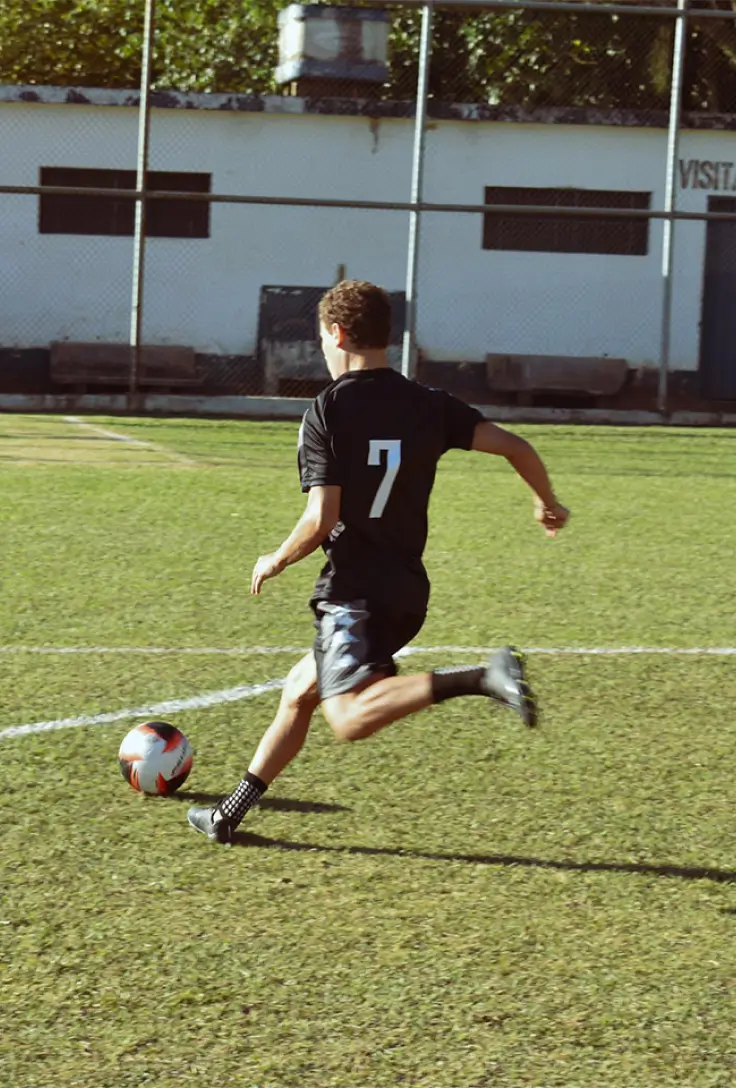 Um jogador de futebol habilidoso controla a bola em um campo verde, vestindo uma camisa preta com o número 7.